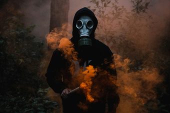 a person wearing a gas mask holding a stick with orange smoke
