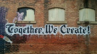 black and white graffiti that says "Together We Create" on a brick building