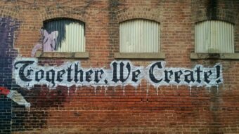 black and white graffiti that says "Together We Create" on a brick building