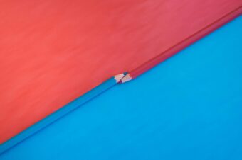 Two intersecting red and blue pencils on a split red and blue background, symbolizing the delicate balance of building trust between a team and an organization.