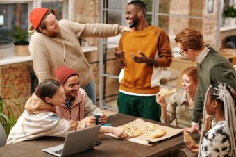 A diverse group of coworkers shares pizza and engages in friendly conversations, exemplifying questions for getting to know your team